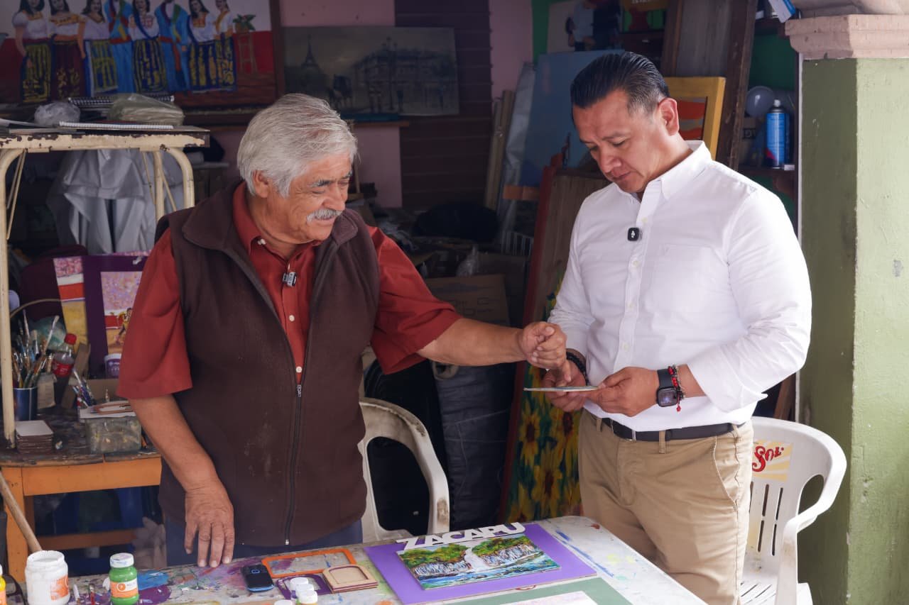 Retrato cercano de Carlos Torres Piña caminando entre personas en una comunidad rural de Michoacán, con gesto serio y cercano, sin micrófonos ni cámaras visibles