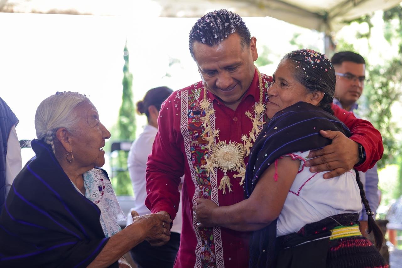 Carlos Torres Piña en diálogo con miembros de una comunidad originaria, en un entorno rural, con gestos de escucha activa y cercanía