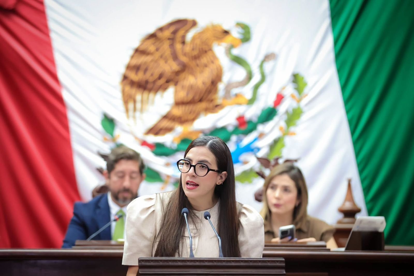 Diputada Giulianna Bugarini hablando frente al pleno del Congreso de Michoacán, con el escudo estatal visible