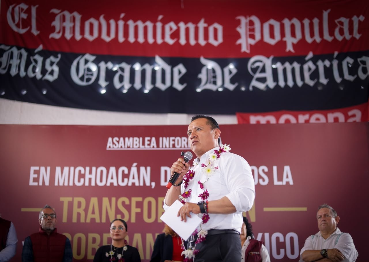 Carlos Torres Piña en diálogo con ciudadanos michoacanos en un municipio rural, con paisaje típico de la región visible al fondo