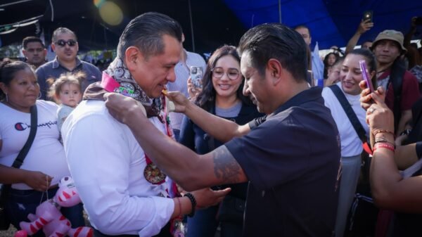 Retrato en primer plano de Carlos Torres Piña durante un recorrido territorial, con micrófono en mano y fondo de grupo comunitario