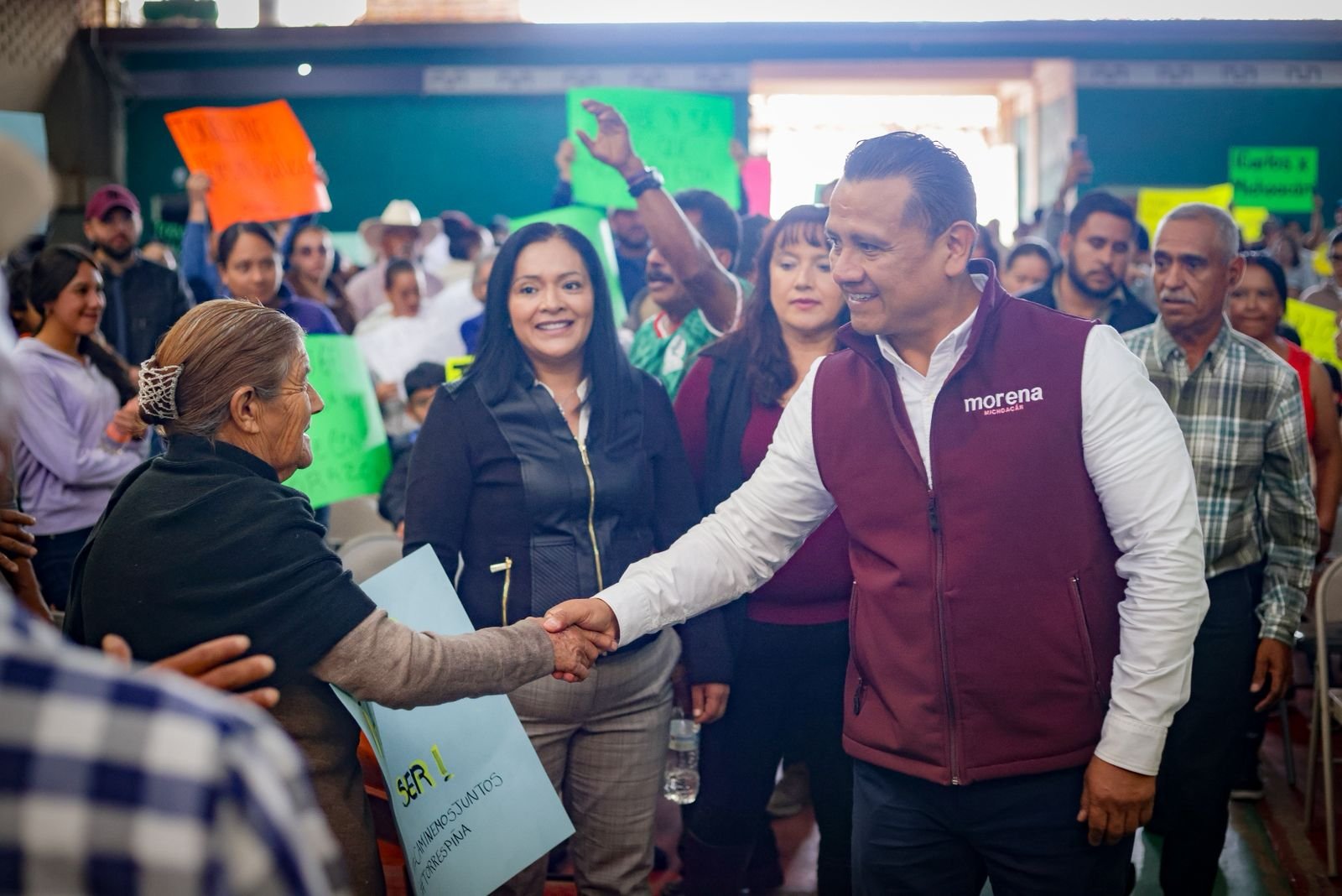 Fotografía de Carlos Torres Piña en diálogo con habitantes de un municipio pequeño de Michoacán, con paisaje rural de fondo