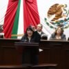 Retrato formal de la diputada Ana Vanessa Caratachea Sánchez hablando en tribuna del Congreso de Michoacán, con bandera estatal al fondo