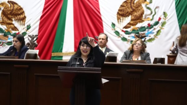 Retrato formal de la diputada Ana Vanessa Caratachea Sánchez hablando en tribuna del Congreso de Michoacán, con bandera estatal al fondo