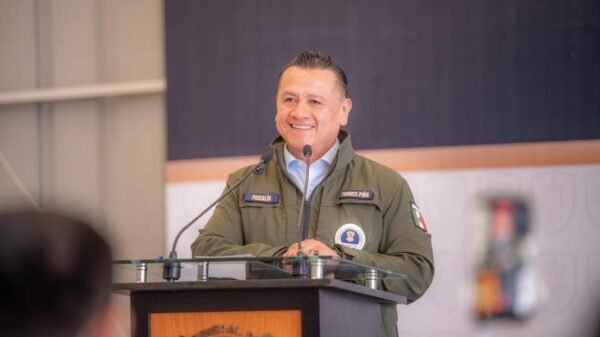 Retrato formal de Carlos Torres Piña frente a un fondo con los logos de la Fiscalía General de Michoacán y el escudo estatal