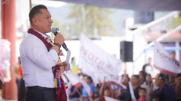 Carlos Torres Piña hablando ante micrófonos y bandera mexicana en un evento público en Morelia, Michoacán