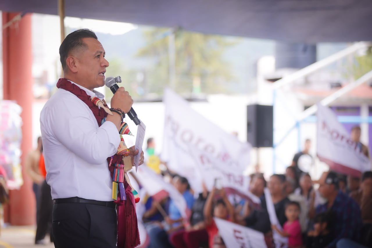 Carlos Torres Piña hablando ante micrófonos y bandera mexicana en un evento público en Morelia, Michoacán