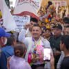 Carlos Torres Piña en una asamblea comunitaria en Michoacán, escuchando a ciudadanos en un espacio abierto, con fondo rural y presencia de personas de distintas edades.