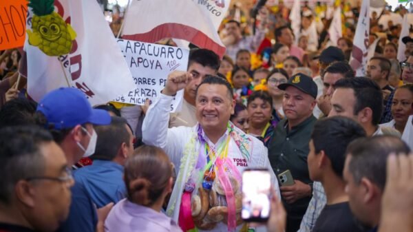 Carlos Torres Piña en una asamblea comunitaria en Michoacán, escuchando a ciudadanos en un espacio abierto, con fondo rural y presencia de personas de distintas edades.