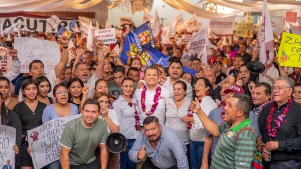 Carlos Torres Piña hablando ante micrófono en evento público en Morelia, Michoacán, con logo de 'Plan Michoacán por la Paz y la Justicia' visible en fondo