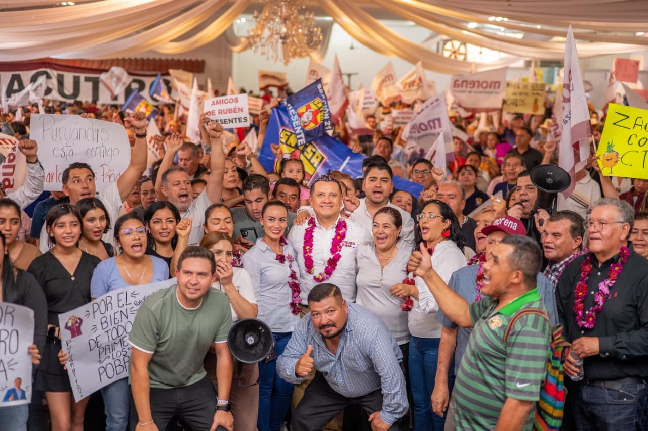 Carlos Torres Piña hablando ante micrófono en evento público en Morelia, Michoacán, con logo de 'Plan Michoacán por la Paz y la Justicia' visible en fondo