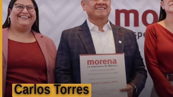 Carlos Torres Piña michoacán hablando frente a una bandera de Morena y símbolos de la transformación, en un acto público en