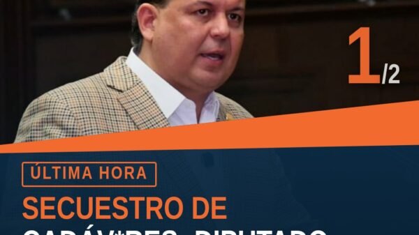 Diputado Memo Valencia hablando ante micrófono en el Congreso del Estado de Michoacán, con fondo de bandera estatal y