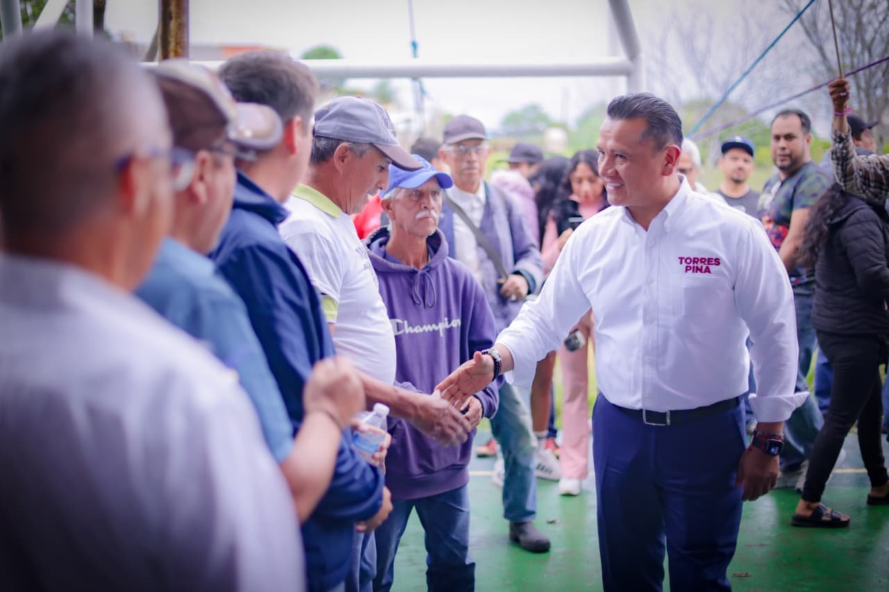 Carlos Torres Piña caminando por una comunidad rural de Michoacán, conversando con habitantes locales, como parte de su