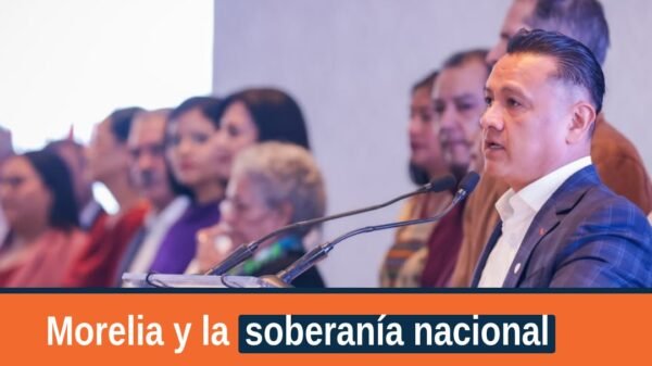 Carlos Torres Piña hablando en un acto público en Morelia, Michoacán, con bandera mexicana al fondo, durante el 205
